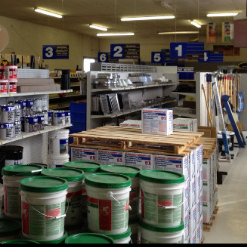 A hardware store interior with shelves filled with paint buckets, tools, and supplies. Overhead signs numbered 1 to 6 guide customers. Bright lighting.