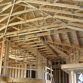 Interior view of a house under construction, showcasing wooden beams and trusses in the ceiling.