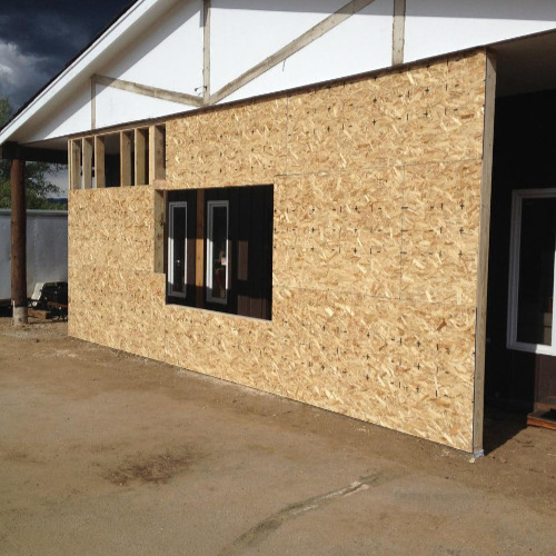 Building under renovation with plywood facade, white trailer nearby, and orange safety netting in front. Sky is partly cloudy, creating a work-in-progress feel.