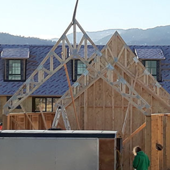 A partially constructed wooden frame of a building with a person working nearby.