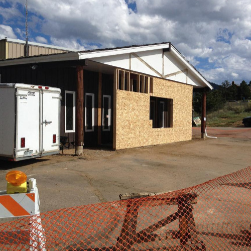 Building under renovation with plywood facade, white trailer nearby, and orange safety netting in front. Sky is partly cloudy, creating a work-in-progress feel.