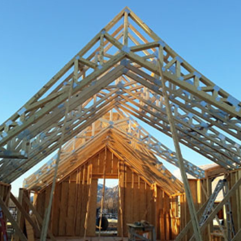 A partially constructed building with a wooden framework and roof trusses against a clear blue sky.