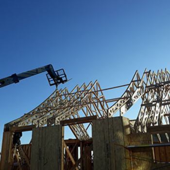 A construction site showing a building framework with a crane lifting materials against a clear blue sky.