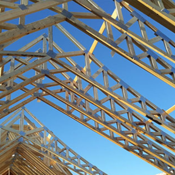 Wooden trusses of a building under construction against a clear blue sky.
