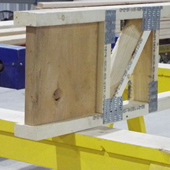 A close-up view of a wooden frame with metal brackets, positioned on a yellow workbench.