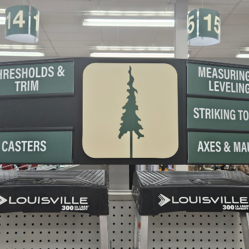 Store aisle signage with a tree icon, displaying sections for thresholds, trim, measuring tools, and axes. Louisville ladders below.