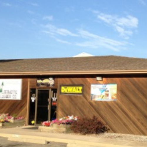Exterior of a building with a wood-paneled facade under a blue sky. Signs include 