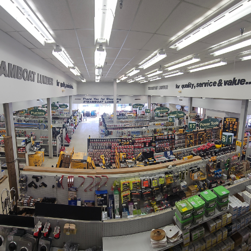 Wide-angle view of a well-lit hardware store with aisles filled with tools, paint, and home improvement supplies. Overhead signs guide shoppers.