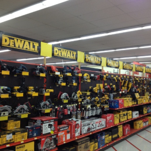 A store aisle filled with DeWalt power tools, including drills and saws, neatly displayed on shelves. Bright yellow signage highlights the brand.