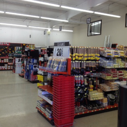 Interior of a hardware store with organized aisles of tools and supplies. Clearance sign reads 