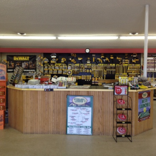 A hardware store's tool section features a wooden counter with various products and brochures. Behind, shelves neatly display yellow-handled tools.