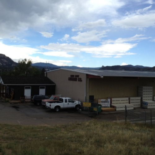 Industrial building under a cloudy sky with mountains in the background. White truck and materials are in the foreground, conveying a rustic, serene setting.