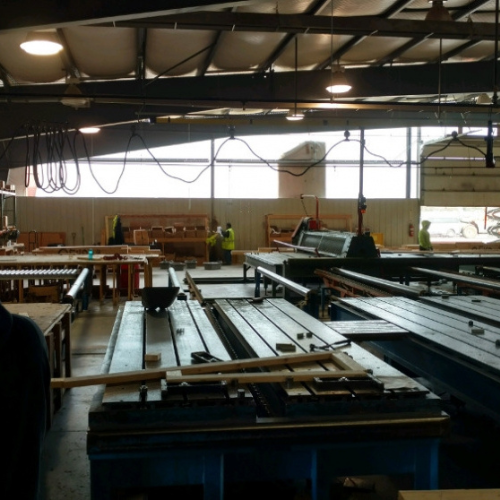 Interior of a large, dimly lit warehouse with conveyor belts and industrial machinery. Workers in safety vests operate equipment in the background.