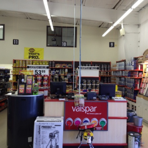 Hardware store interior with a Valspar paint display at the counter. Paint cans and supplies line the shelves. Bright lighting, organized layout.