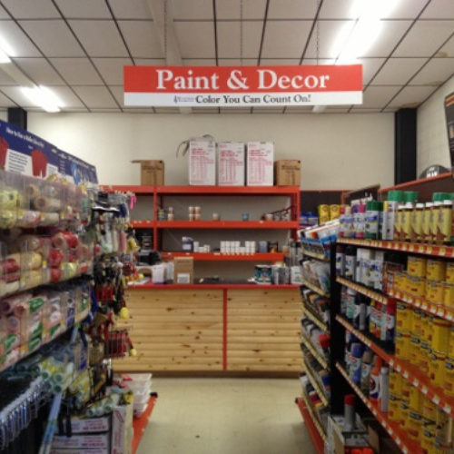 Paint and decor aisle in a store, with colorful paint cans and supplies on shelves. A sign above reads 