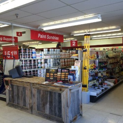 Interior of a hardware store with shelves of paint cans and supplies. A rustic wooden counter displays tools. Bright, organized, and inviting.