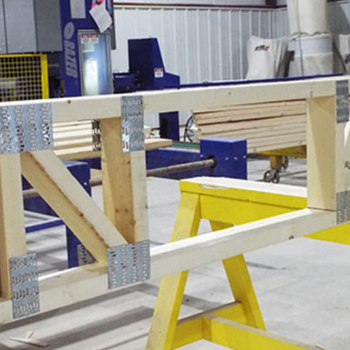 A wooden frame under construction in an industrial workspace, with metal brackets securing the joints.