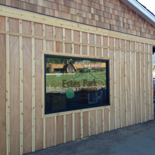 Wooden building facade with vertical planks and a large rectangular window displaying a blurred logo. Sunny day, calm and rustic feel.
