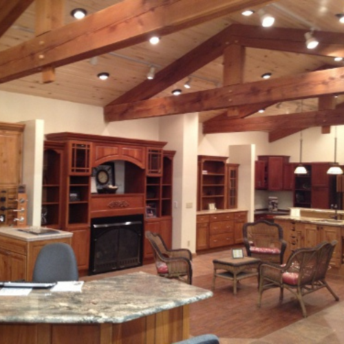 Rustic kitchen with exposed wooden beams, warm lighting, and wood cabinetry. Features include wicker chairs, a stone countertop, and a cozy seating area.