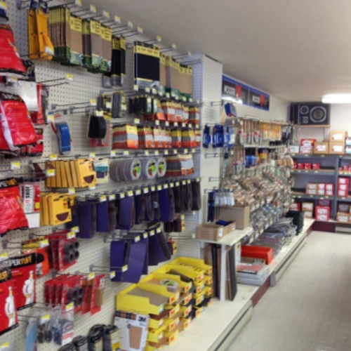 A hardware store aisle displaying assorted sandpaper, tools, and supplies on wall racks and shelves. The setting is organized and utilitarian.