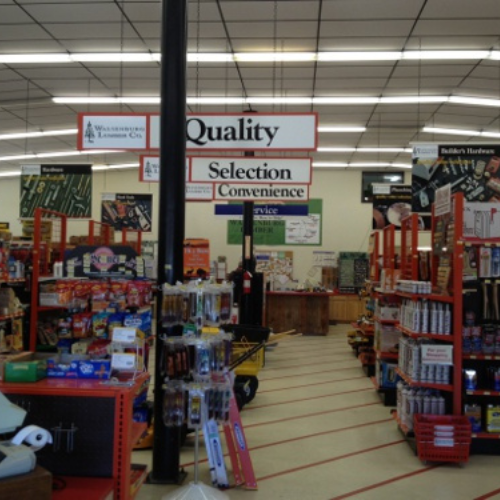 A hardware store interior with aisles of tools and supplies. Overhead signs read 