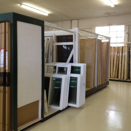 Interior of a hardware store; racks display doors and window frames neatly arranged. The setting is bright and organized, conveying a sense of order.