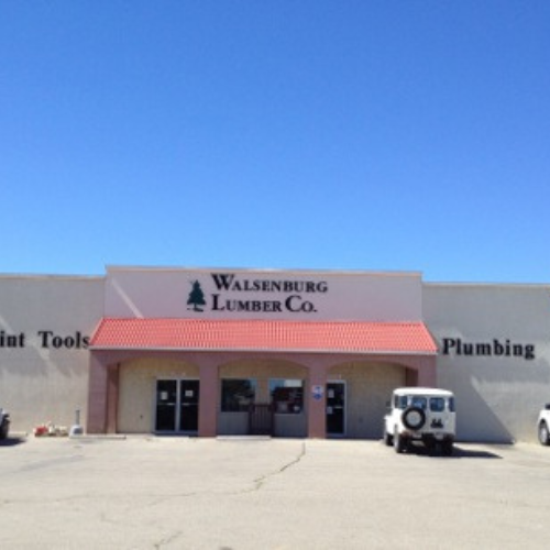 The image shows the exterior of Walsenburg Lumber Co., a hardware store with a red roof and beige walls. A vintage white vehicle is parked outside.