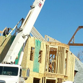Construction site with a crane and workers on a partially built wooden structure.