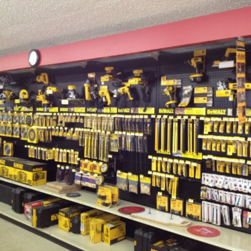 Wall-mounted display of neatly organized yellow and black tools in a hardware store. Various power tools and accessories create a professional and orderly atmosphere.