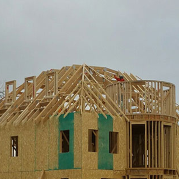 A partially finished house under construction, featuring wooden framing and green sheathing on the exterior.