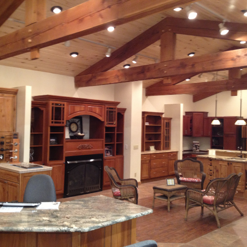 Spacious rustic kitchen with exposed wooden beams, warm lighting, dark wood cabinets, wicker furniture, and a stone countertop, creating a cozy ambiance.