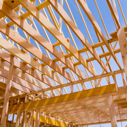 Roof TrussesWooden house frame under construction, viewed from beneath against a clear blue sky. The structure reveals intersecting beams, suggesting progress and growth.
